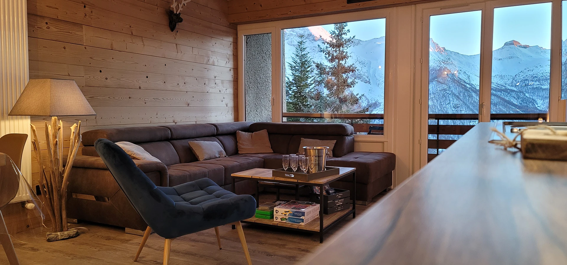 Salon ambiance chalet de haute montagne, grand canapé et fauteuil bleu avec superbe vue sur la montagne enneigée