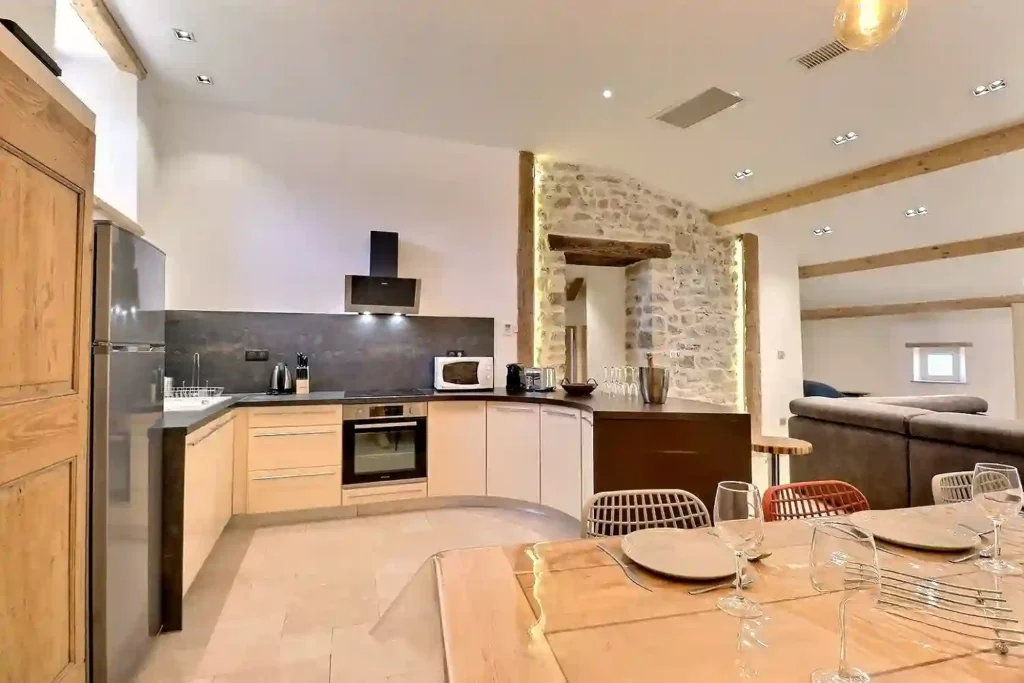 Cuisine moderne tout équipée au Gîte Le Figuier à Gras avec table à manger et mur en pierre.