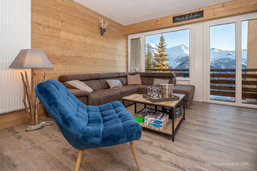 Salon de l'appartement Horizon 1800 à Orcières avec vue sur les montagnes exposé plein sud, son grand canapé et son fauteuil bleu