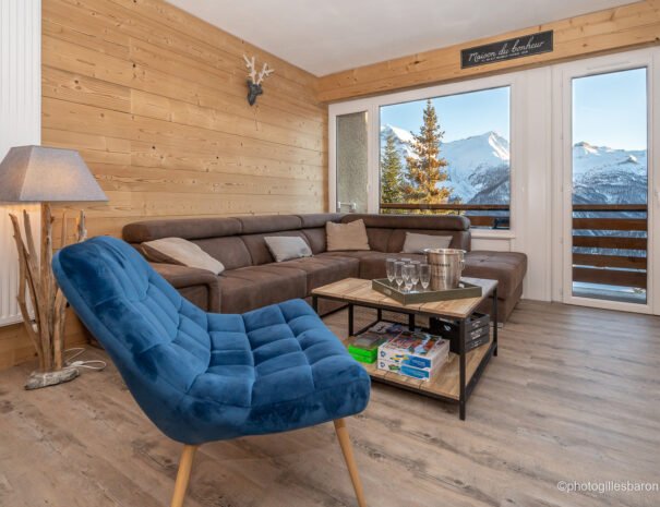 Salon de l'appartement Horizon 1800 à Orcières avec vue sur les montagnes exposé plein sud, son grand canapé et son fauteuil bleu