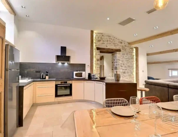 Cuisine moderne tout équipée au Gîte Le Figuier à Gras avec table à manger et mur en pierre ainsi que son bar.